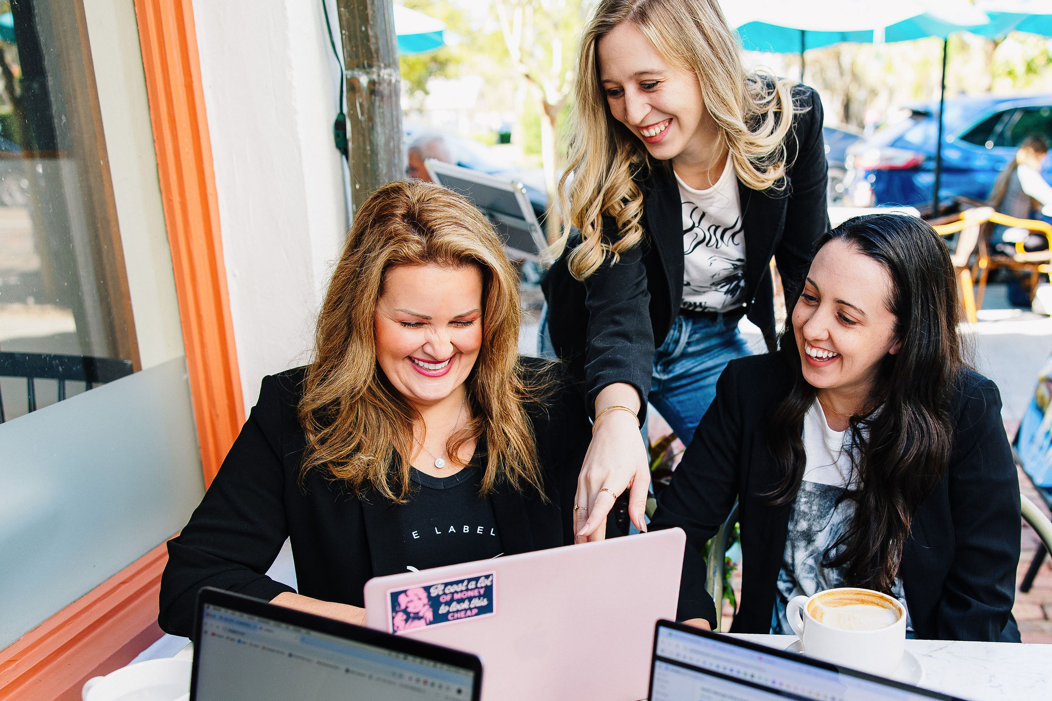 Three energized female working professionals working on laptops at coffee shop.