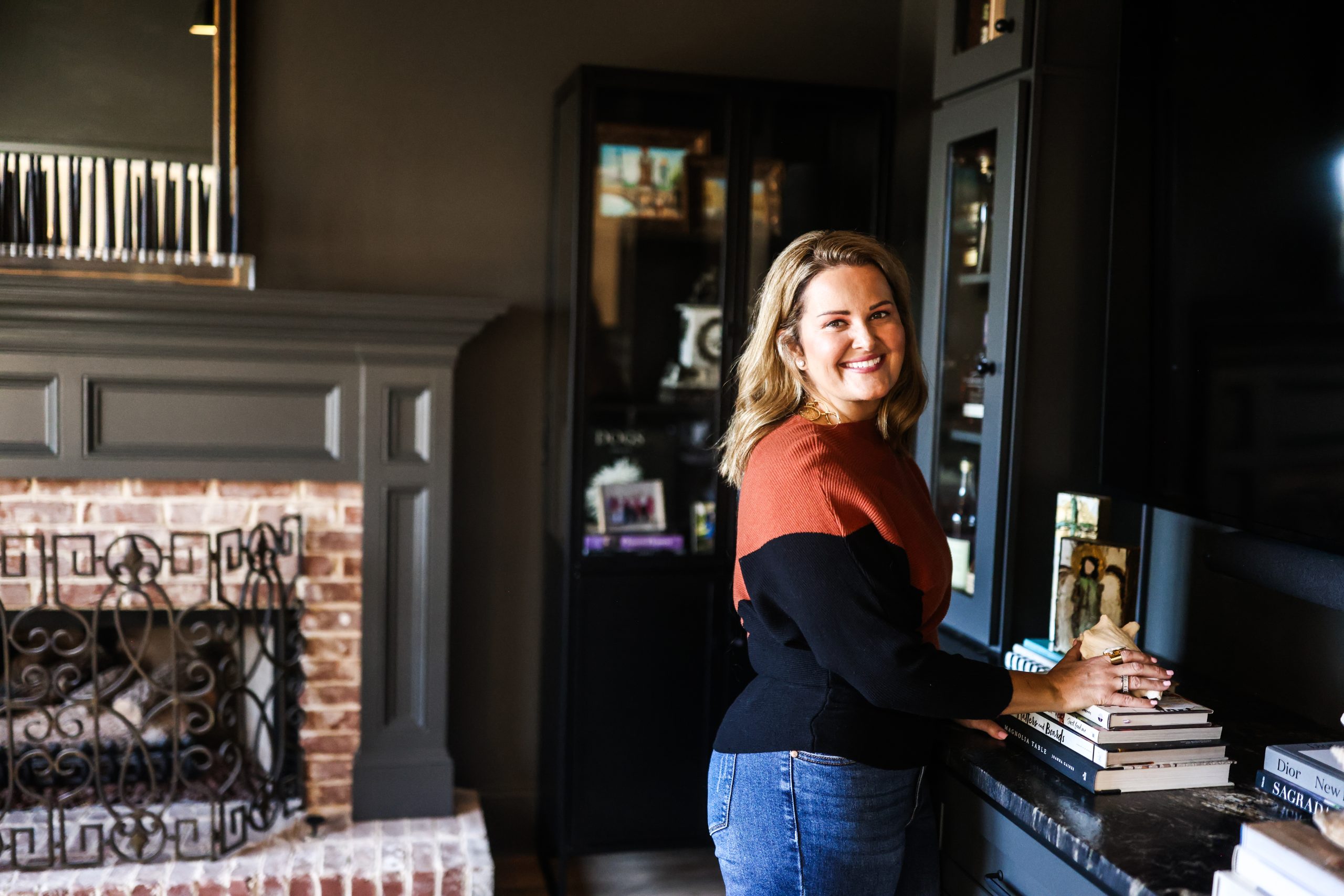 Mollie Surratt in the color-drenched keeping room, painted in Sherwin Williams Urbane Bronze with a brick fireplace and black built-ins