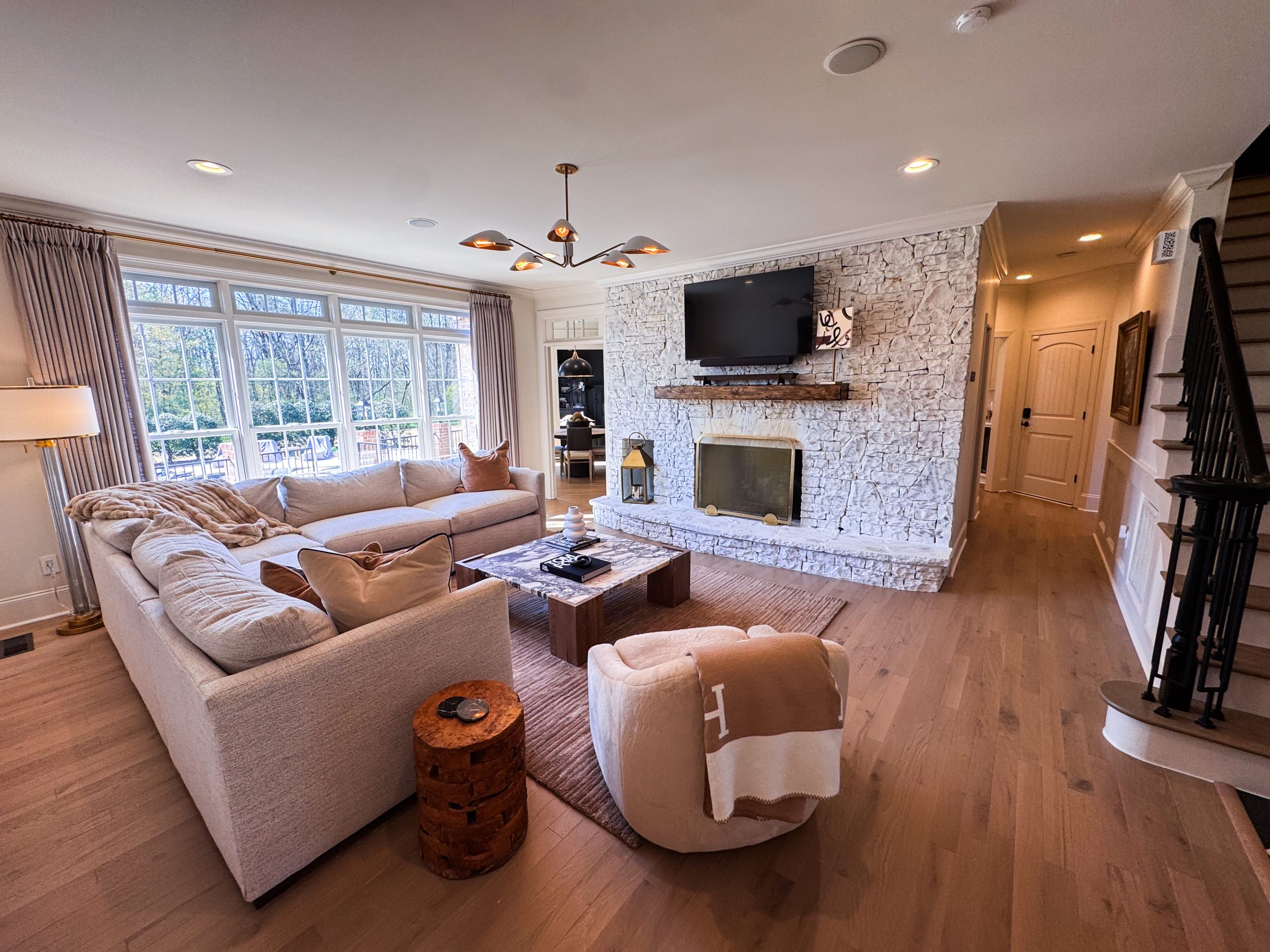 Wide view of the renovated Living Room with painted stone fireplace, mounted TV, and blonde engineered hardwood floors