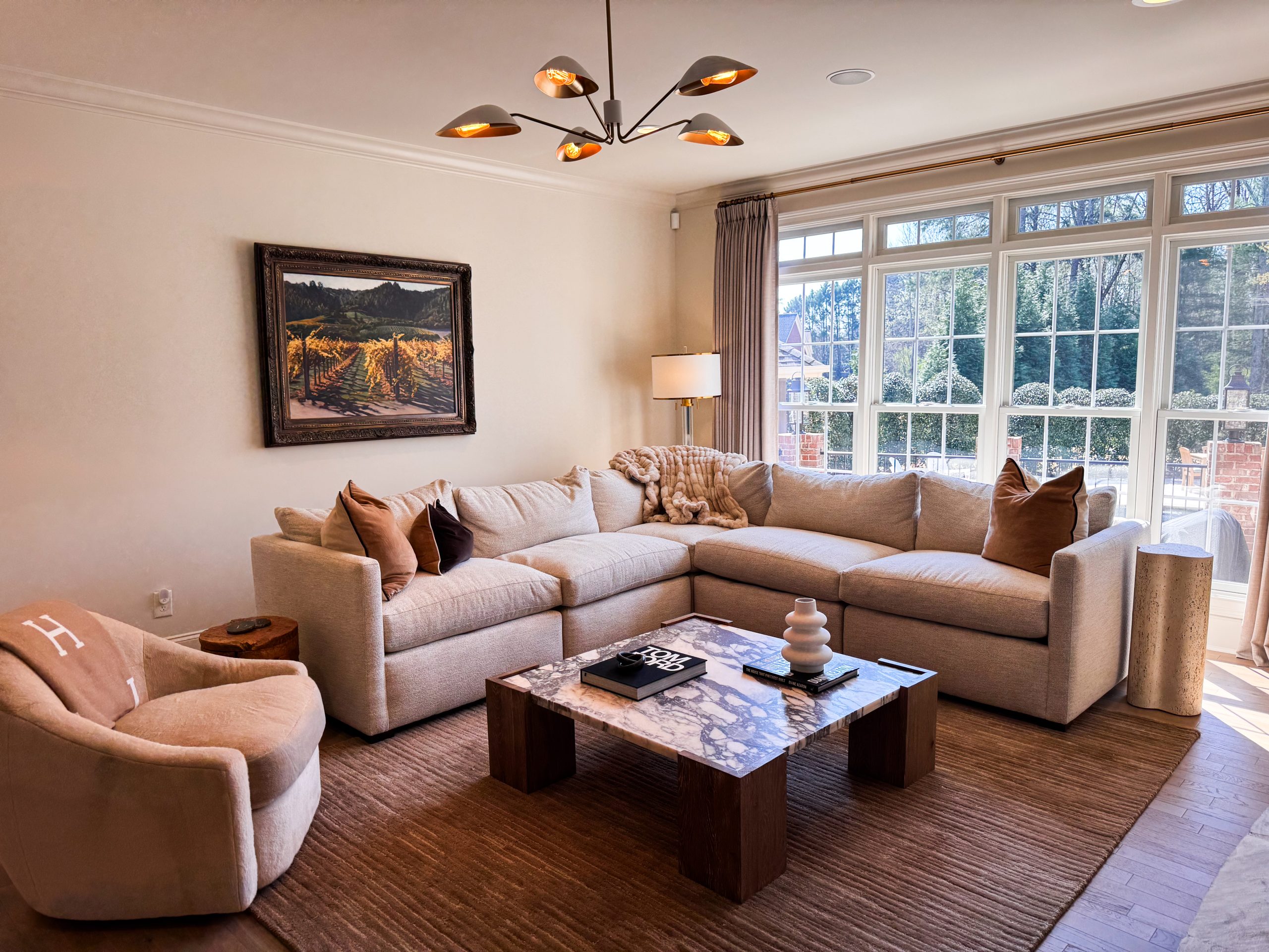 Wide view of the Living Room with the original Napa Valley painting above the sectional and a modern chandelier overhead