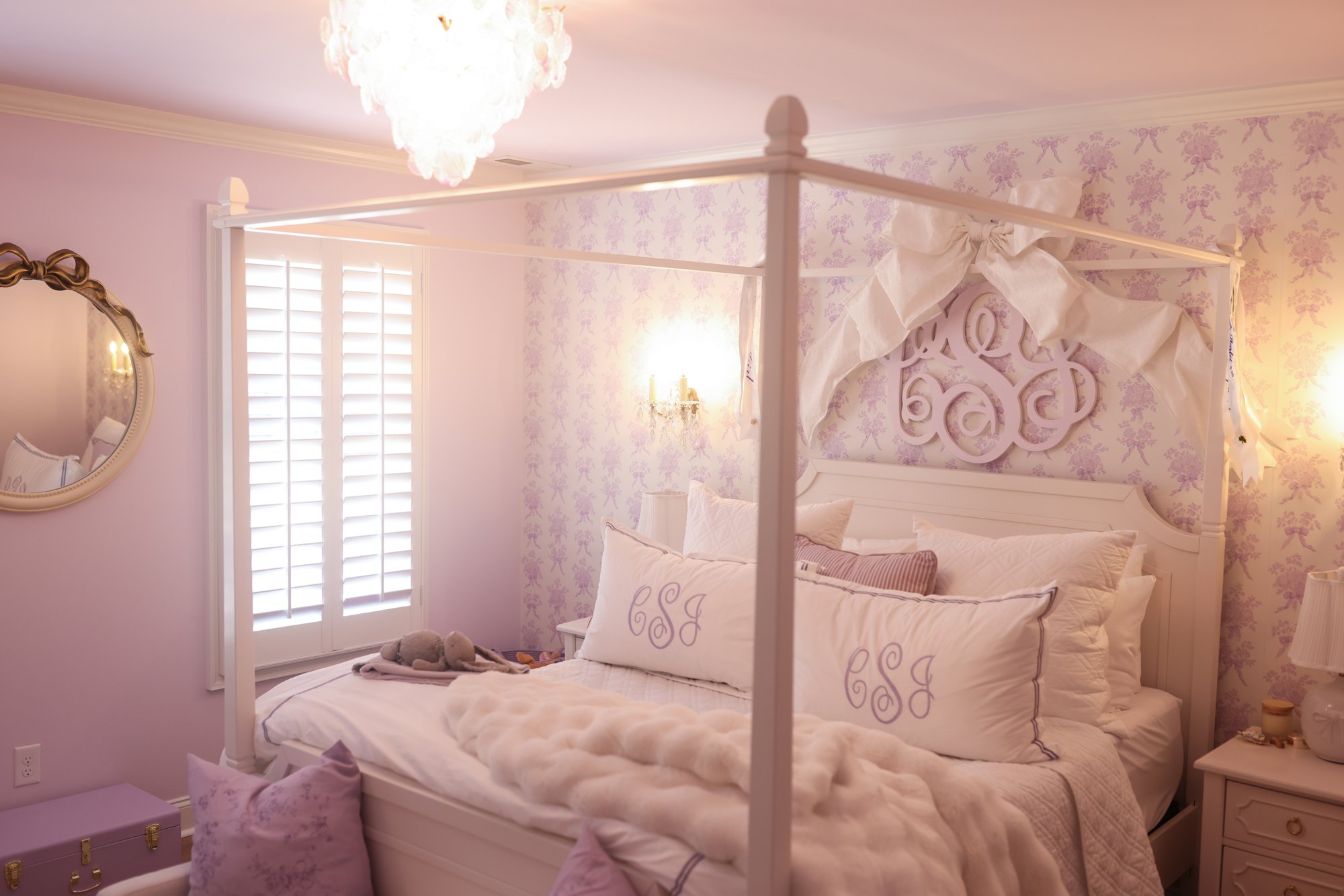 White canopy bed with a monogrammed headboard and lavender pillows in Charlotte's bedroom