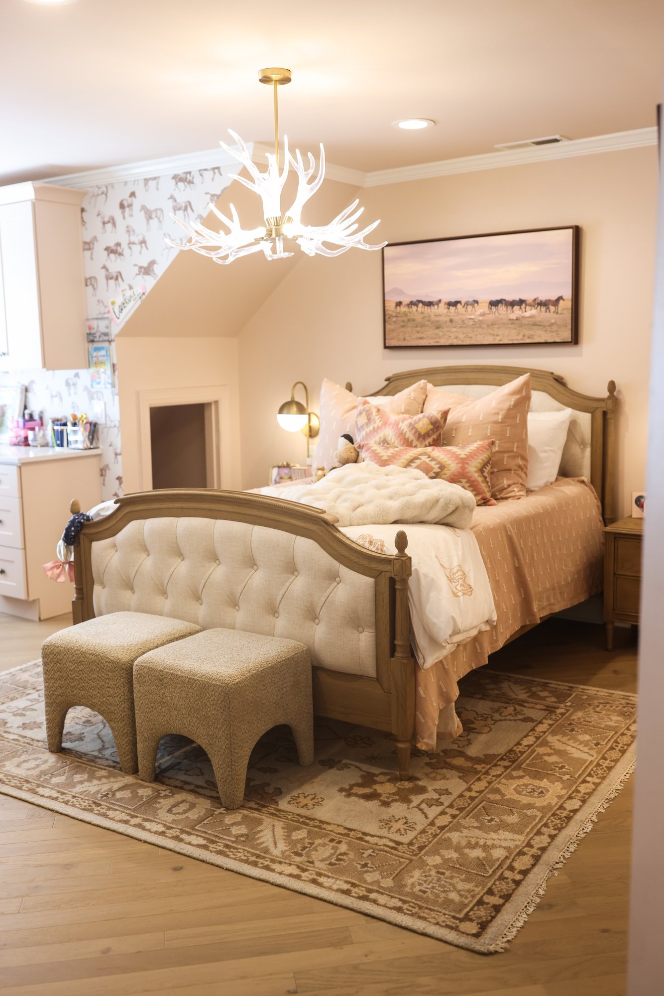 Tufted upholstered bed with dusty rose bedding and an antler chandelier in Caroline's bedroom