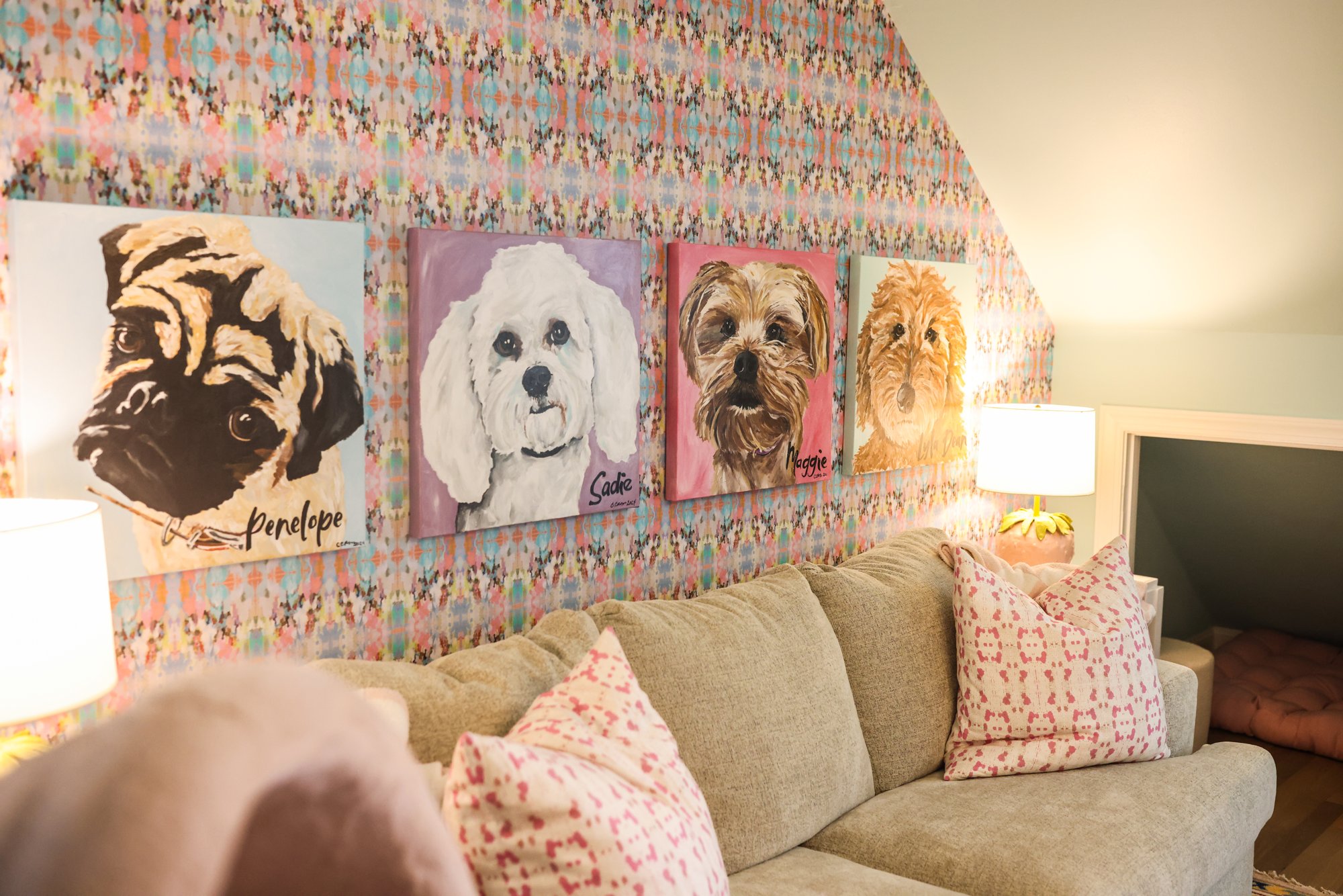 Colorful wallpaper, custom dog portraits, and pink pillows above the playroom sofa