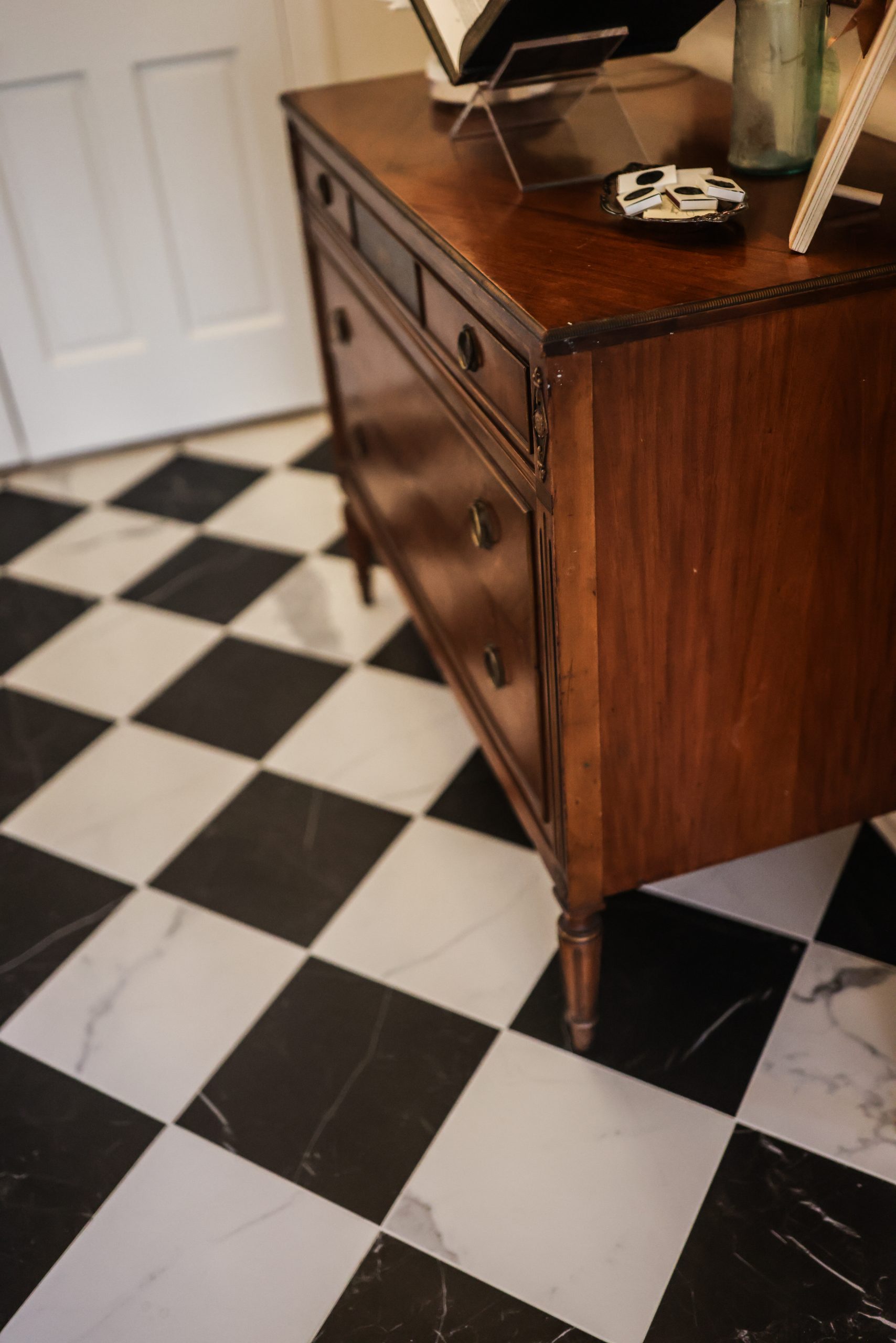 Antique dresser styled with books and keepsakes atop black-and-white checkered marble tile in a home entryway