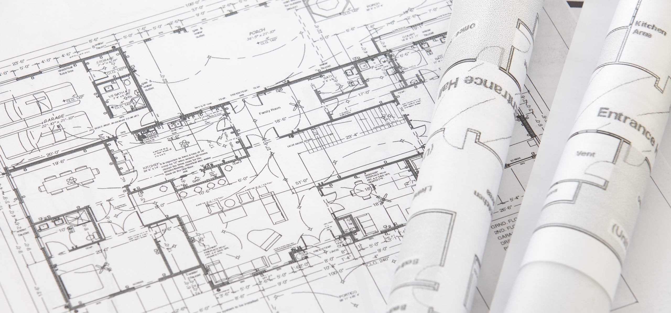 Rolled architectural blueprints and floor plans spread across a table, representing the technical specifications a home brand's marketing partner needs to understand